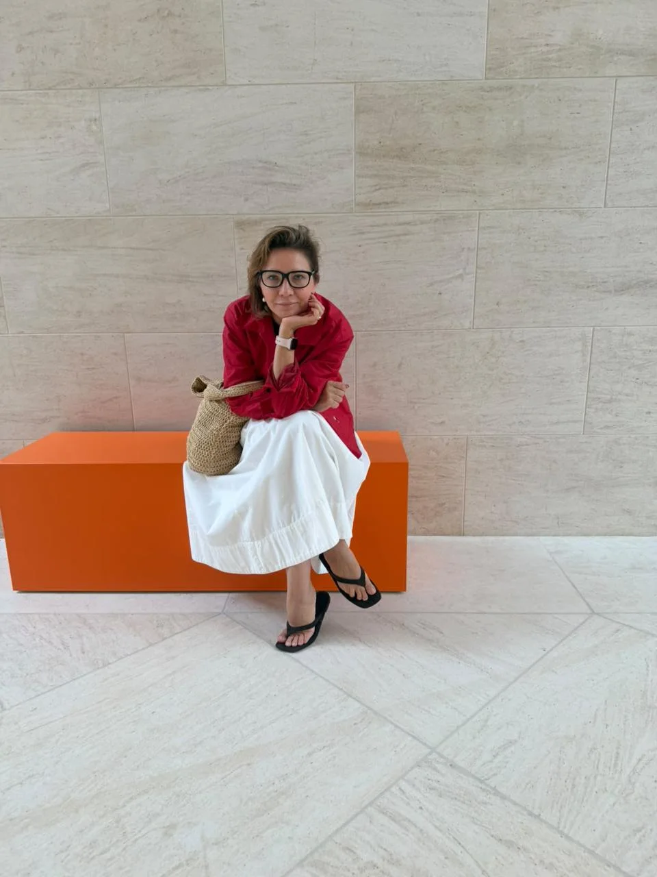 Elena Krasnykh seated on an orange bench in a stone-clad gallery foyer